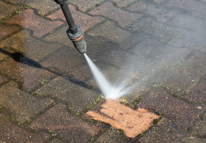 A closeup of a paver driveway in the process of being pressure washed.