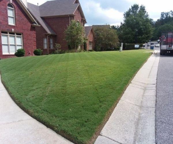A residential brick home with a large front lawn that has been freshly mowed.