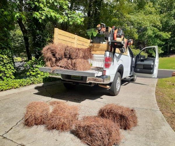 Bales of pine straw being unloaded from the back of a Parsonic Services work truck.